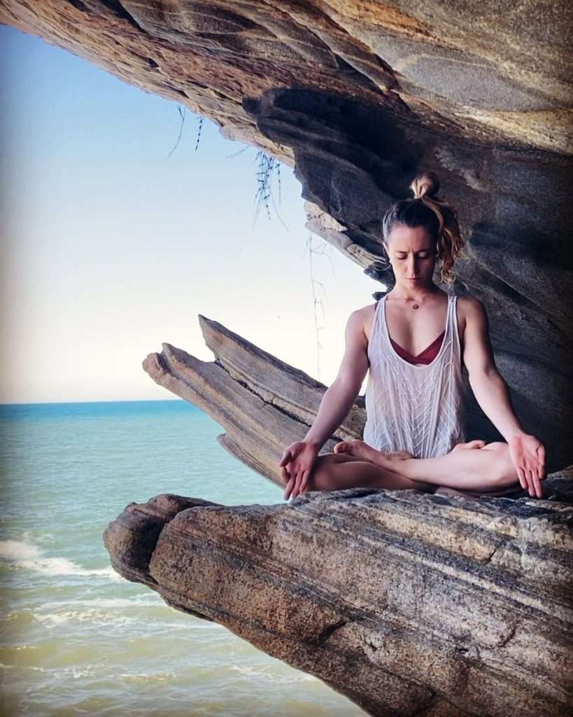 Julia Raboni instrutora de Ashtanga Yoga em Saquarema está meditando na pedra na frente do mar