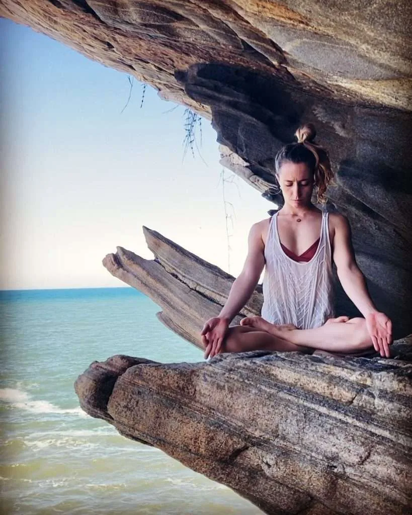 Julia Raboni instrutora de Ashtanga Yoga em Saquarema está meditando na pedra na frente do mar